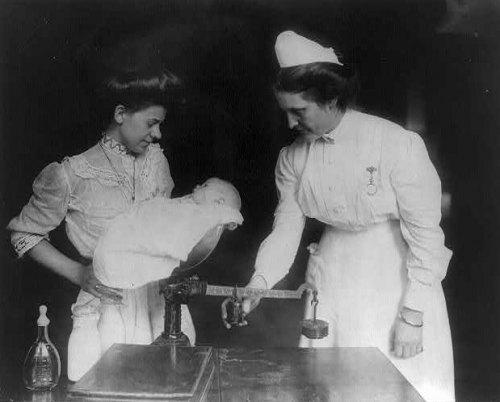 Nurses weigh a newborn baby at a milk station.